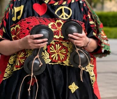 Nahaufnahme von Händen mit zwei Paar eisernen Qraqeb vor einem schwarzen Kaftan mit roten und goldenen Blumenstickereien
