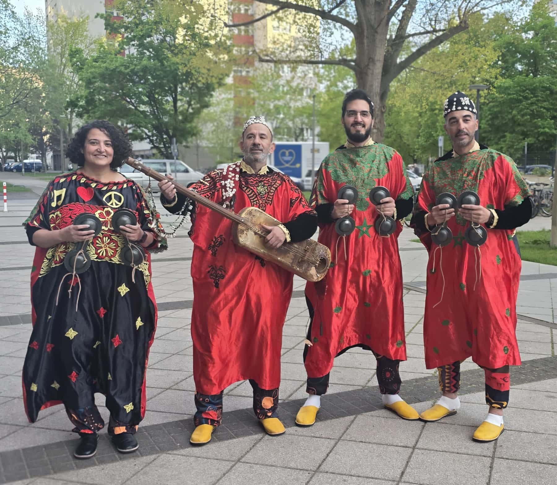 Four members of the band stand on a Berlin pavement, one holding a guembri, the others qraqeb